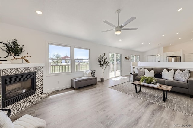 living room with ceiling fan, lofted ceiling, light wood-type flooring, and a tiled fireplace