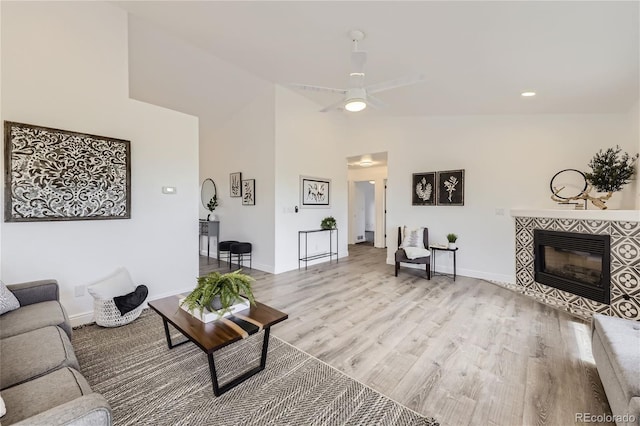 living room featuring ceiling fan, light hardwood / wood-style floors, vaulted ceiling, and a tiled fireplace