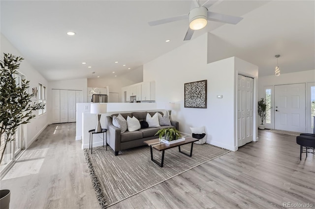 living room with ceiling fan, light hardwood / wood-style floors, and vaulted ceiling