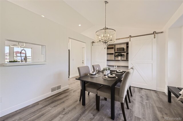 dining area featuring a chandelier, wood-type flooring, a barn door, and high vaulted ceiling