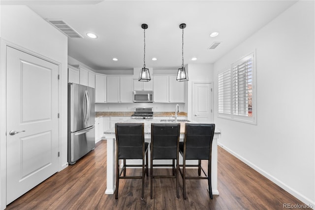 kitchen featuring a breakfast bar, white cabinetry, pendant lighting, stainless steel appliances, and a kitchen island with sink