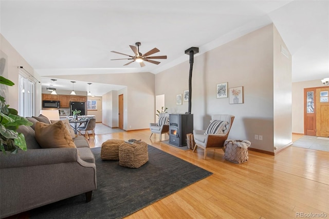 living room with ceiling fan, light hardwood / wood-style floors, a wood stove, and vaulted ceiling