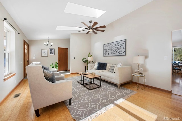 living room with vaulted ceiling with skylight, ceiling fan with notable chandelier, and light hardwood / wood-style floors