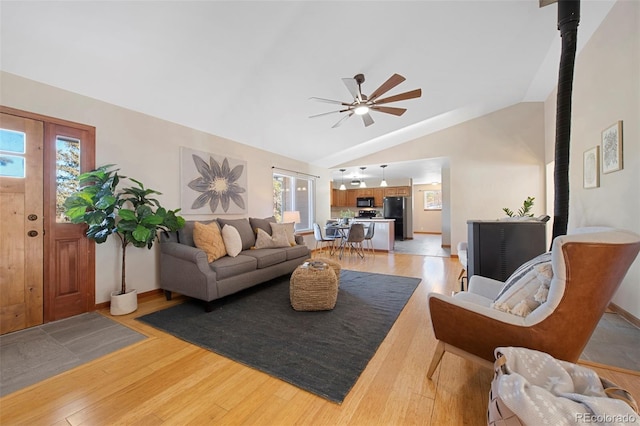 living room with ceiling fan, light hardwood / wood-style floors, and vaulted ceiling