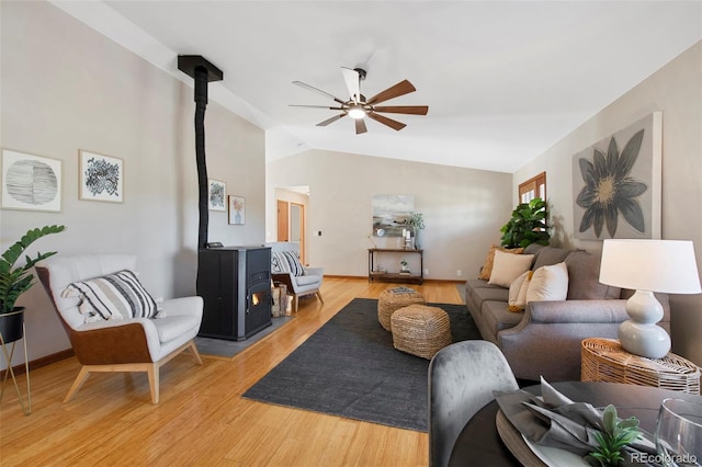 living room with hardwood / wood-style floors, vaulted ceiling, a wood stove, and ceiling fan