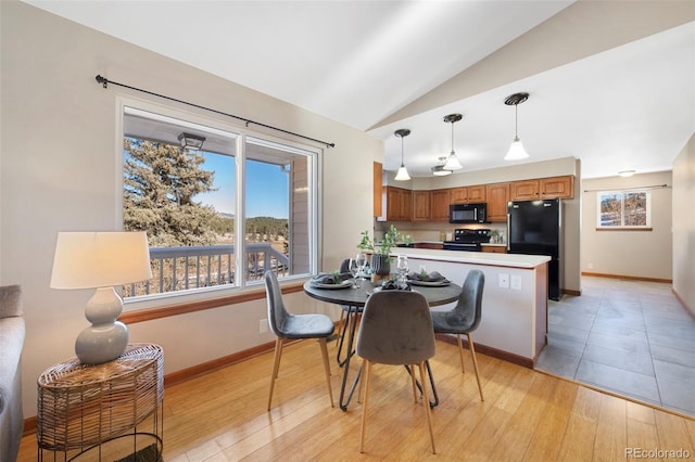 dining room featuring lofted ceiling, light wood-style flooring, and baseboards