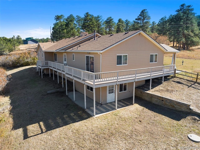 back of property with a shingled roof and a wooden deck