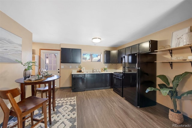 kitchen with light wood-style floors, dark cabinets, light countertops, black appliances, and a sink