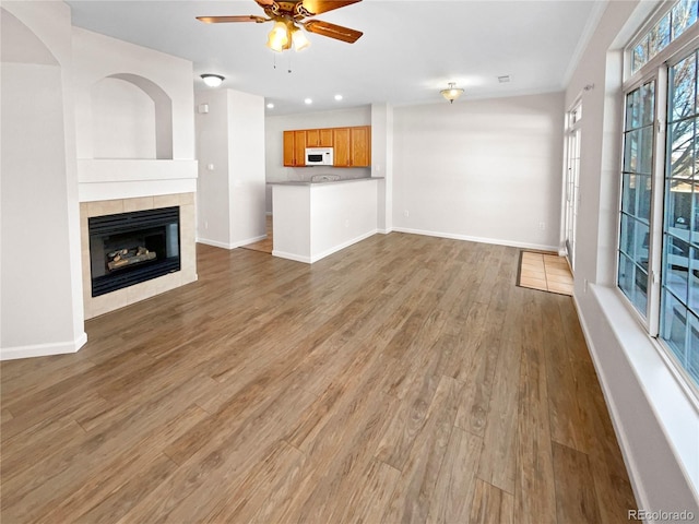 unfurnished living room featuring ceiling fan, crown molding, a fireplace, and hardwood / wood-style floors