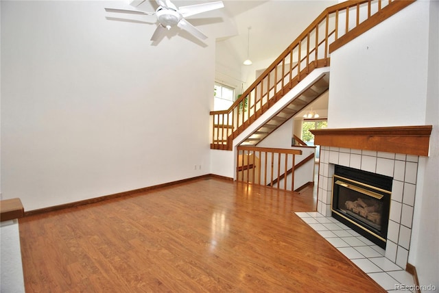 unfurnished living room with a tile fireplace, a towering ceiling, baseboards, and wood finished floors