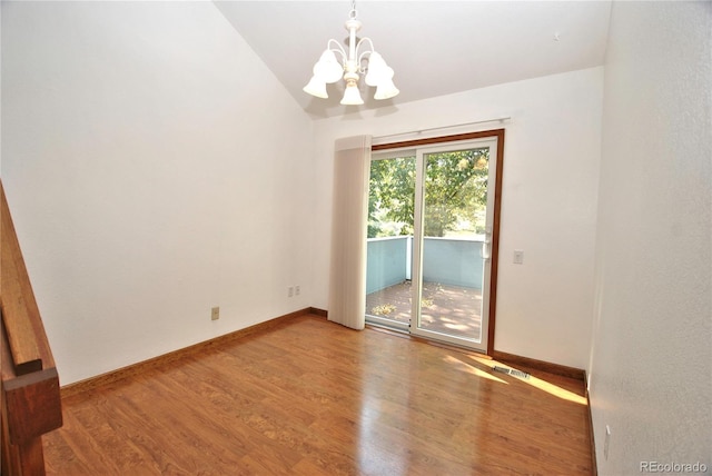 spare room featuring a notable chandelier, visible vents, vaulted ceiling, wood finished floors, and baseboards