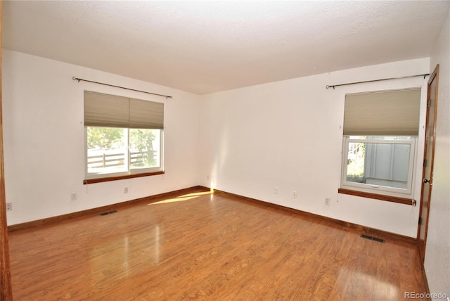 spare room featuring baseboards, visible vents, and wood finished floors