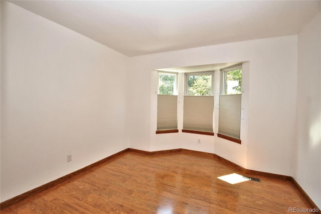 unfurnished room with wood finished floors, visible vents, and baseboards