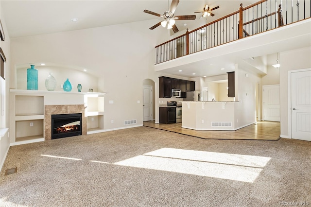 unfurnished living room with a fireplace, carpet flooring, a high ceiling, ceiling fan, and built in shelves