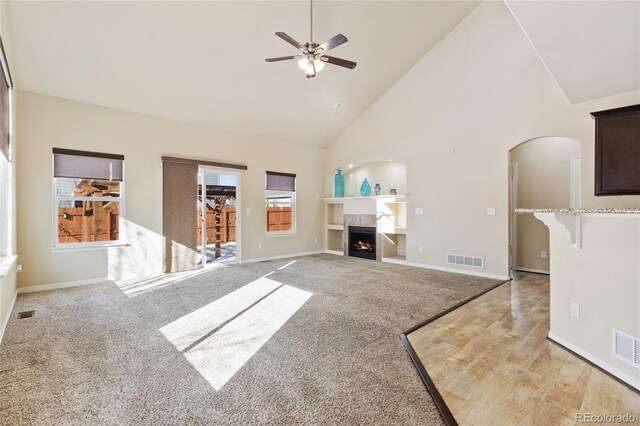 unfurnished living room with a fireplace, a ceiling fan, visible vents, high vaulted ceiling, and arched walkways