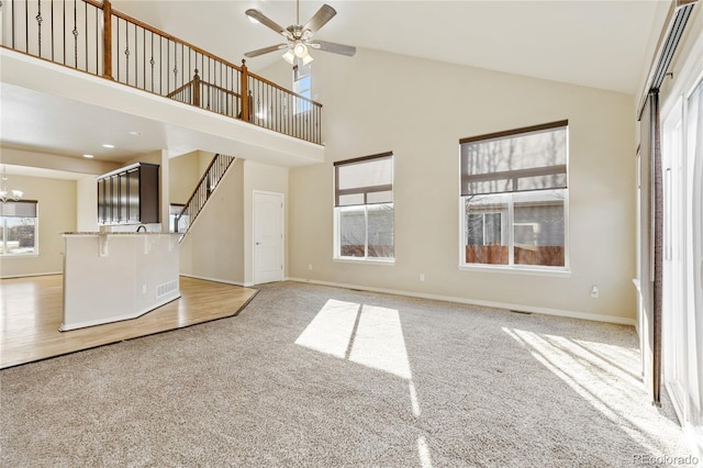 unfurnished living room with light carpet, ceiling fan with notable chandelier, high vaulted ceiling, and baseboards