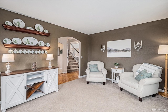 sitting room featuring baseboards, stairway, arched walkways, and light colored carpet