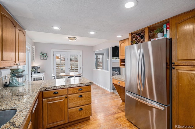 kitchen featuring brown cabinets, tile countertops, light wood-style floors, freestanding refrigerator, and a peninsula