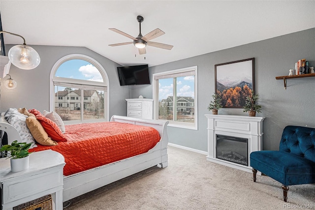 carpeted bedroom with lofted ceiling, a glass covered fireplace, a ceiling fan, and baseboards