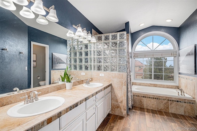 bathroom with a textured wall, toilet, wood tiled floor, vaulted ceiling, and a sink