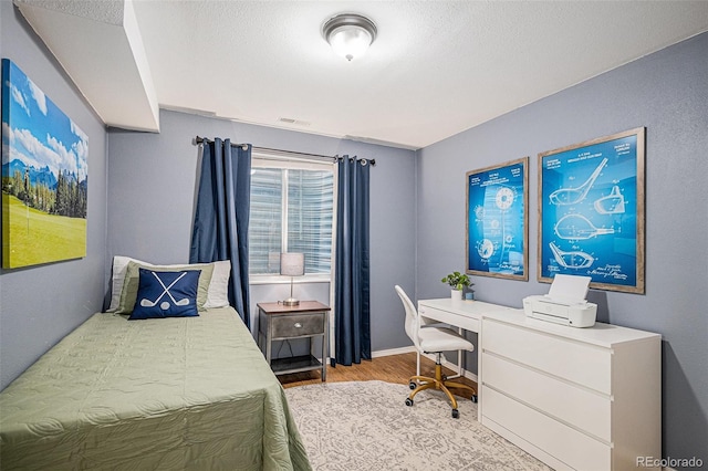 bedroom featuring visible vents, a textured ceiling, baseboards, and wood finished floors