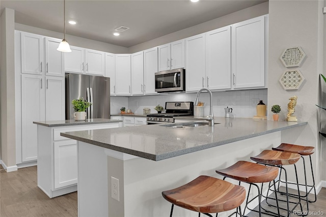 kitchen featuring a breakfast bar, sink, white cabinets, kitchen peninsula, and stainless steel appliances