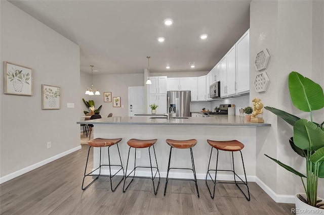 kitchen with a breakfast bar, kitchen peninsula, pendant lighting, stainless steel appliances, and white cabinets