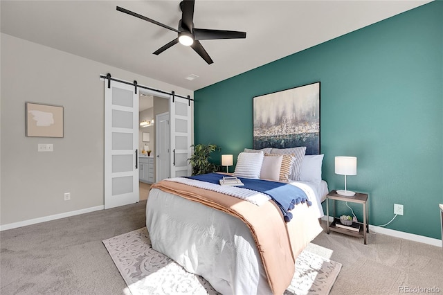 carpeted bedroom with ensuite bath, a barn door, and ceiling fan