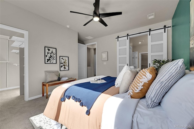 bedroom with carpet flooring, a walk in closet, ceiling fan, a barn door, and ensuite bath