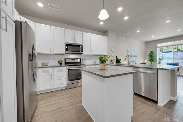 kitchen with a sink, appliances with stainless steel finishes, light wood-type flooring, and a peninsula