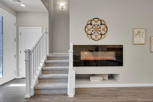 staircase with baseboards, visible vents, and wood finished floors