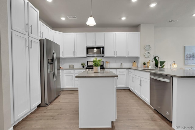 kitchen with light wood finished floors, a peninsula, appliances with stainless steel finishes, and a sink