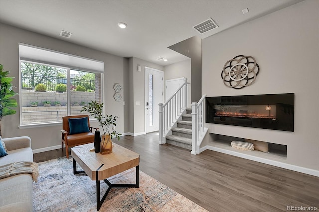 living area with stairs, visible vents, a glass covered fireplace, and wood finished floors