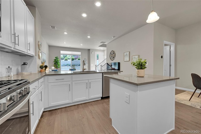 kitchen with a sink, light wood finished floors, a peninsula, and stainless steel appliances