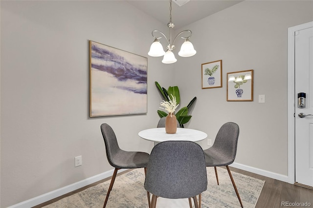 dining space with baseboards, lofted ceiling, wood finished floors, and a chandelier