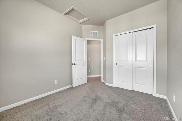 unfurnished bedroom with attic access, carpet, baseboards, visible vents, and a closet