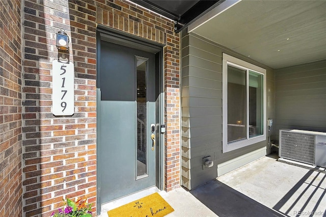 view of exterior entry featuring cooling unit and brick siding