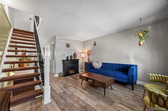 living area featuring wood finished floors, visible vents, baseboards, stairs, and a lit fireplace