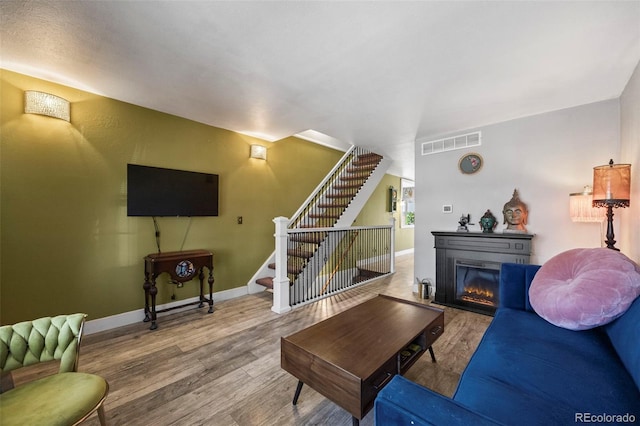 living room featuring visible vents, stairway, a glass covered fireplace, wood finished floors, and baseboards