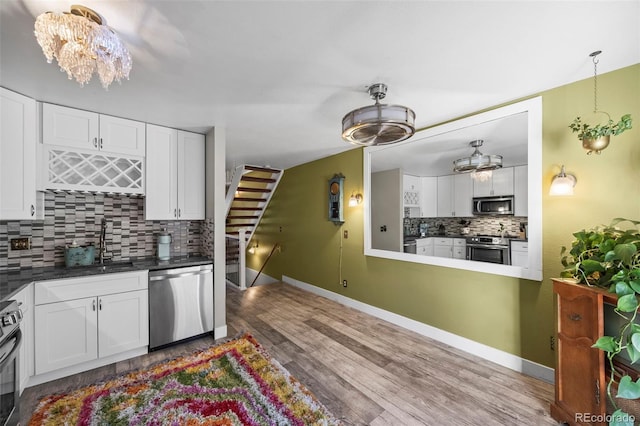 kitchen with tasteful backsplash, white cabinets, appliances with stainless steel finishes, wood finished floors, and a sink