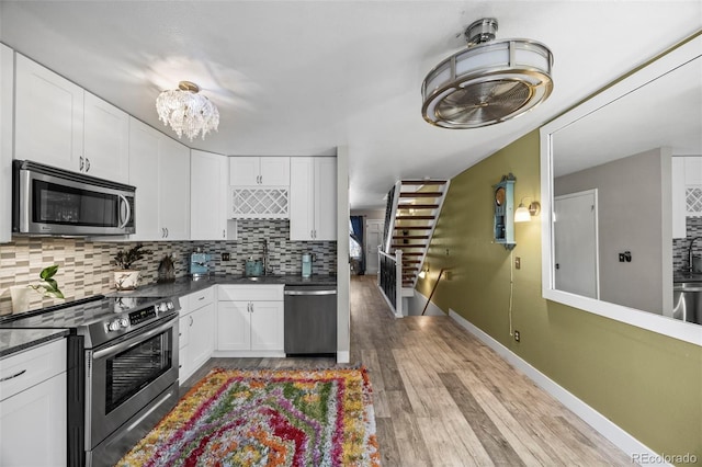 kitchen with light wood finished floors, tasteful backsplash, dark countertops, appliances with stainless steel finishes, and white cabinetry