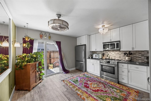 kitchen with light wood-style flooring, stainless steel appliances, white cabinets, tasteful backsplash, and dark countertops