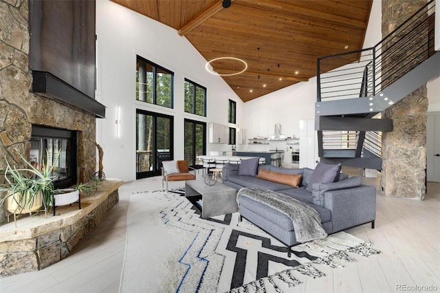 living room with light wood-type flooring, beam ceiling, high vaulted ceiling, wooden ceiling, and a stone fireplace