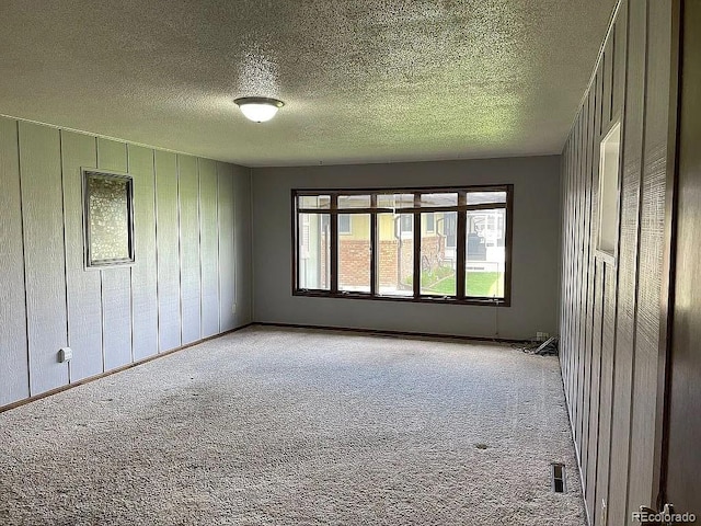 carpeted empty room featuring wooden walls and a textured ceiling