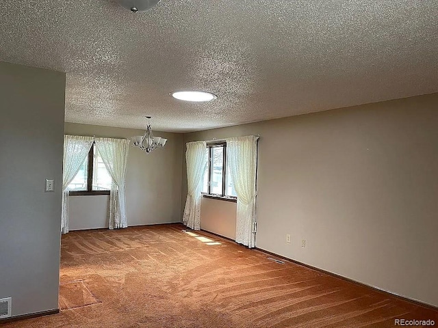 carpeted empty room featuring a textured ceiling, plenty of natural light, and a chandelier