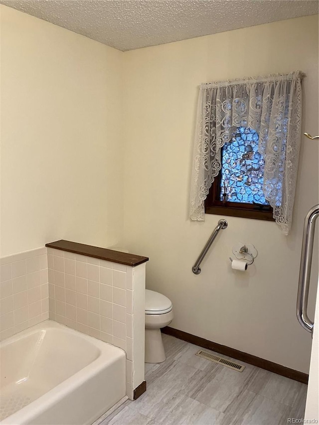 bathroom featuring hardwood / wood-style flooring, toilet, a textured ceiling, and a washtub