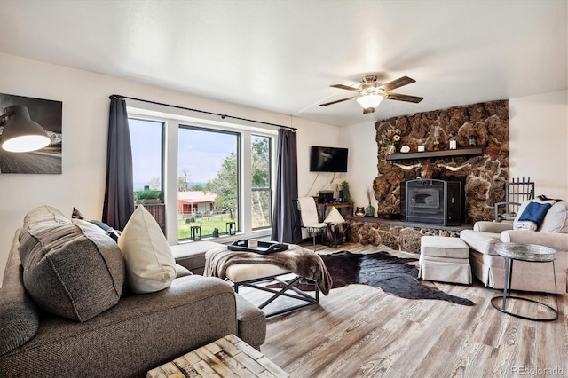 living room featuring ceiling fan, a fireplace, light hardwood / wood-style floors, and a wood stove