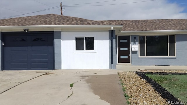 property entrance with brick siding, an attached garage, driveway, and roof with shingles