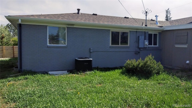 back of house featuring a lawn, brick siding, and a shingled roof