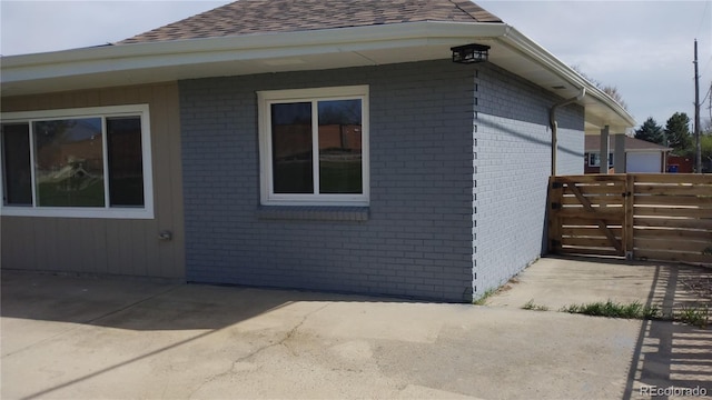 view of side of property with fence, a patio, a shingled roof, and brick siding